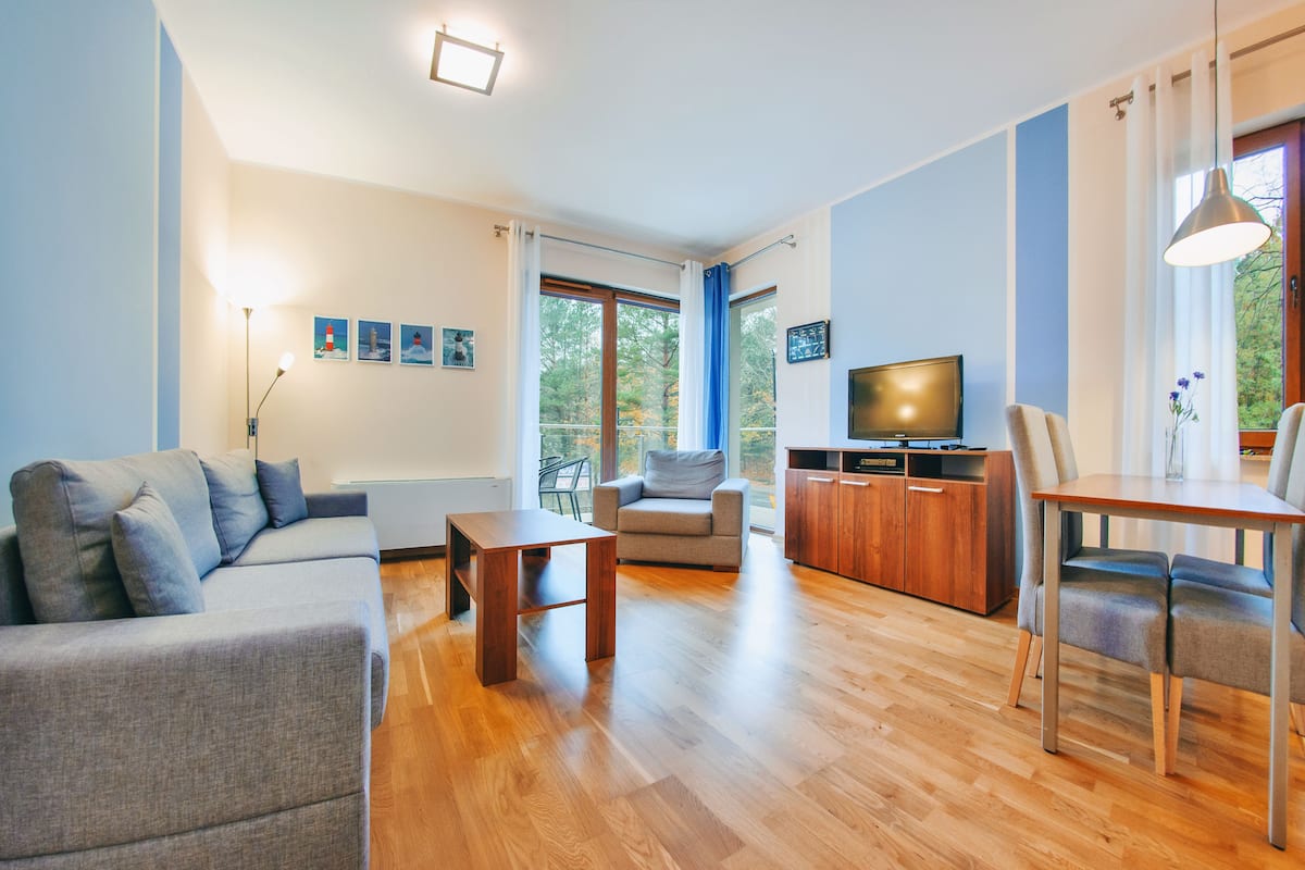 A modern living room with a sofa, a coffee table, a TV, and a dining area with chairs.