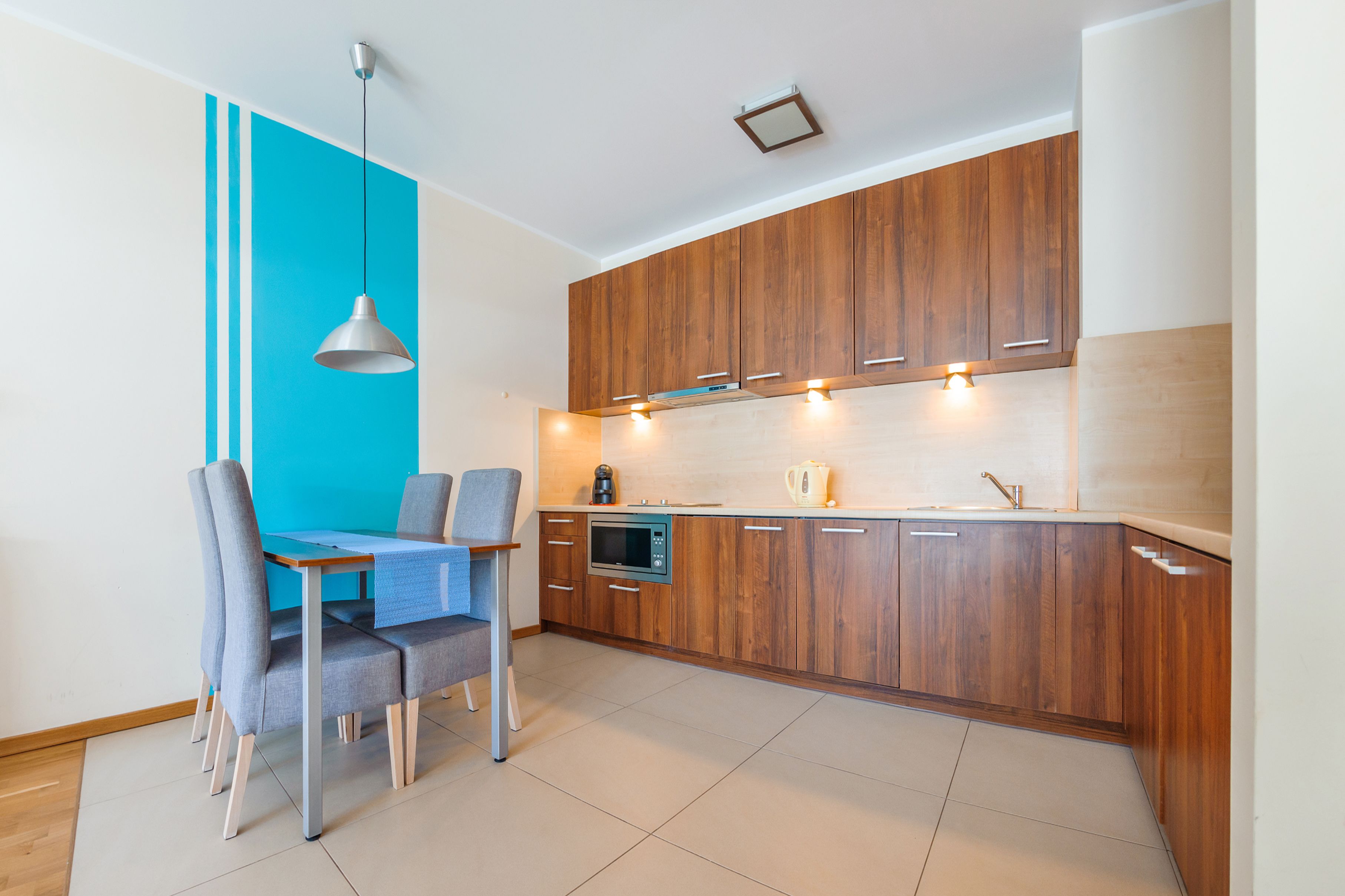 A modern kitchen with wooden cabinets, a built-in oven, and a dining area with a table and chairs.
