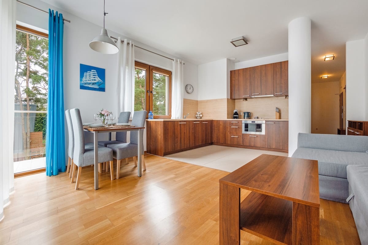 A modern kitchen with wooden cabinets, a dining area with a table and chairs, and a living room with a sofa.