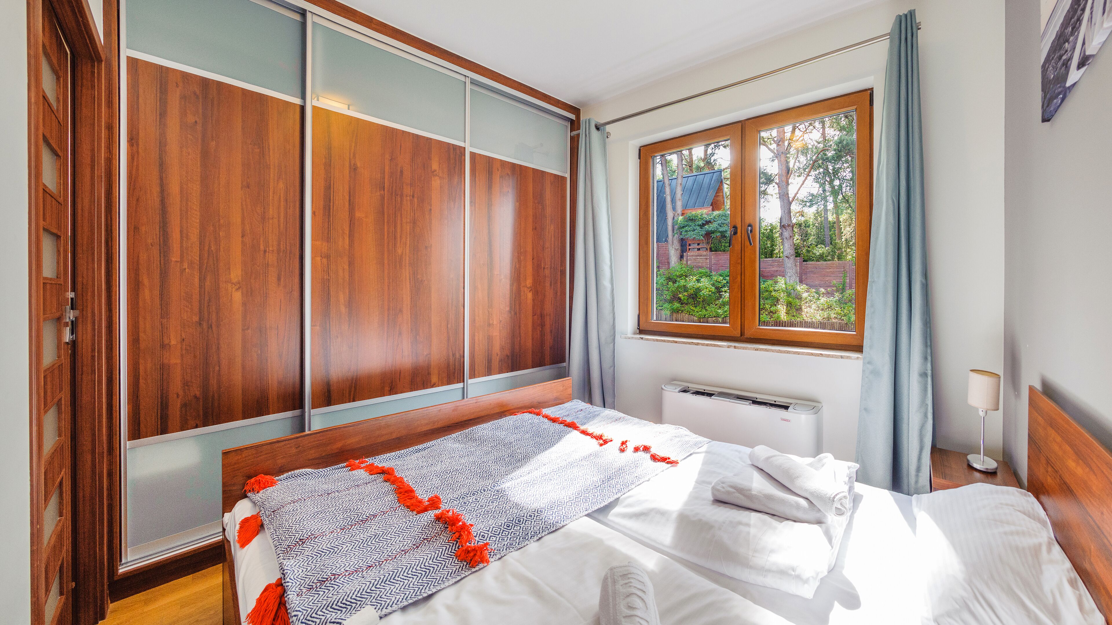 A bedroom with a bed, wooden wardrobe, window with curtains, and a radiator.