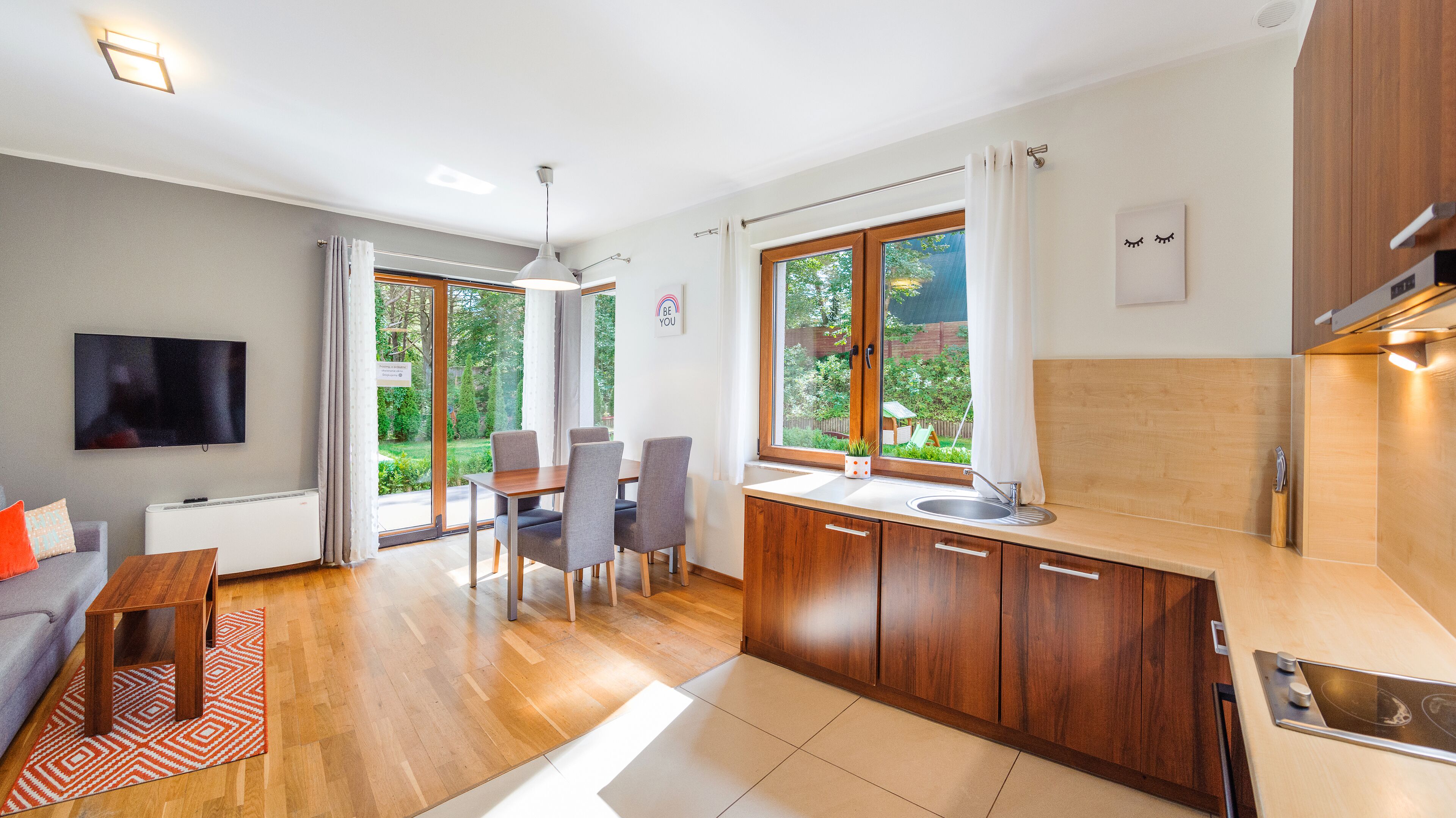 A modern kitchen with wooden cabinets, a built-in oven, and a window overlooking a garden.