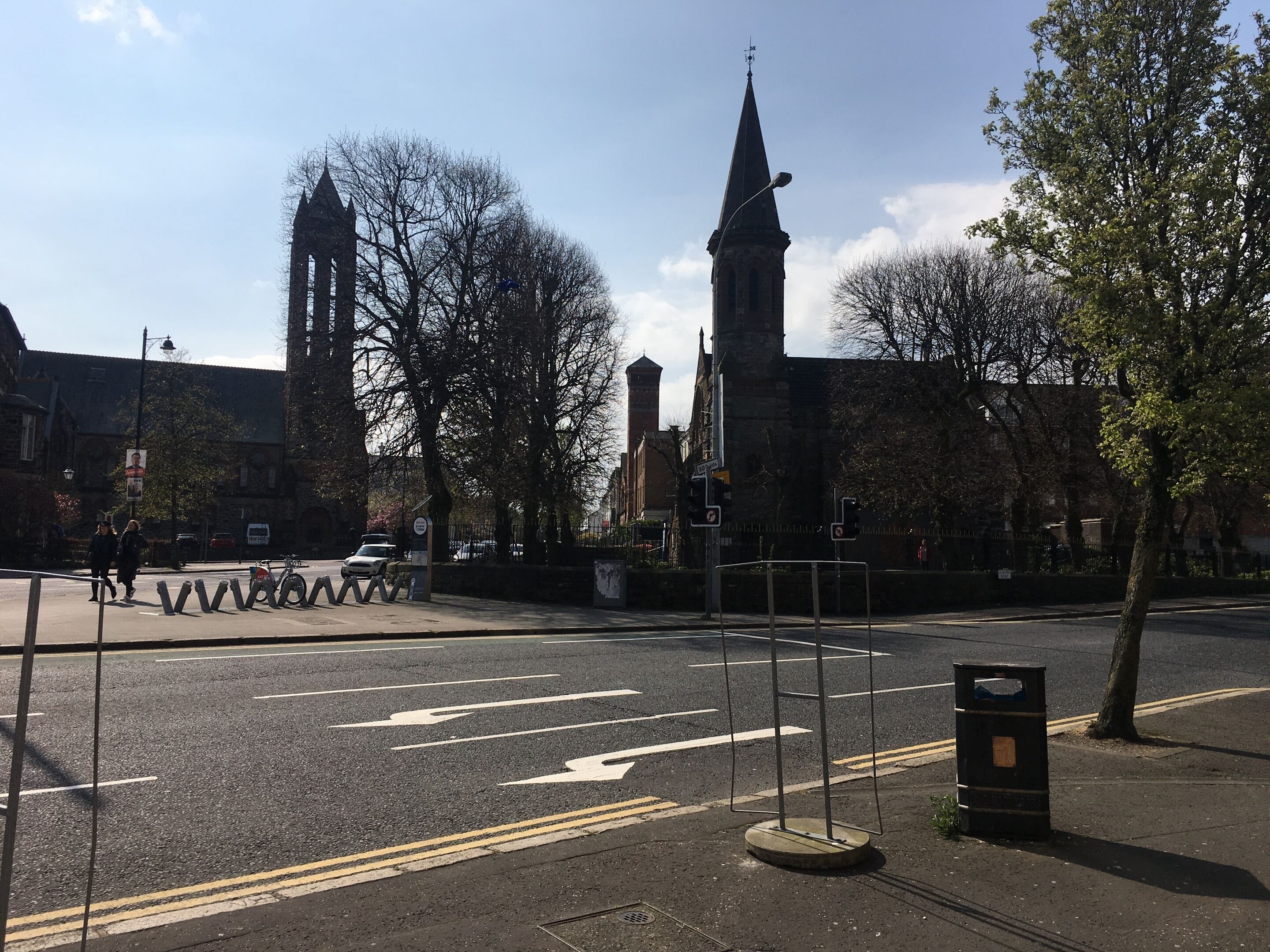 Een straatovergang met een kerktoren, een fietsenrek en een afvalbak.