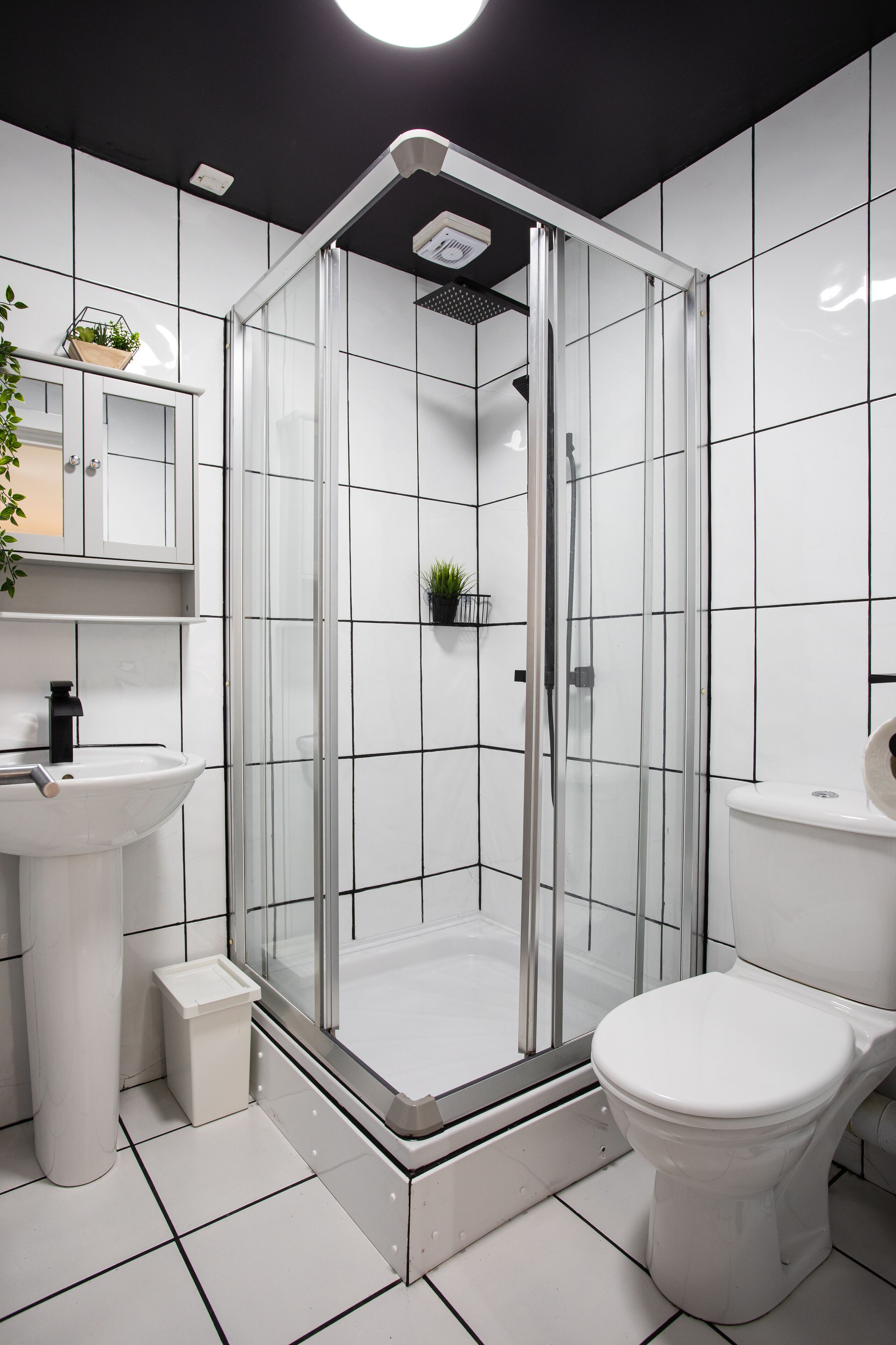 Een moderne badkamer met een douche met glazen wand, witte tegels, een wit wastafelmeubel en een toilet.