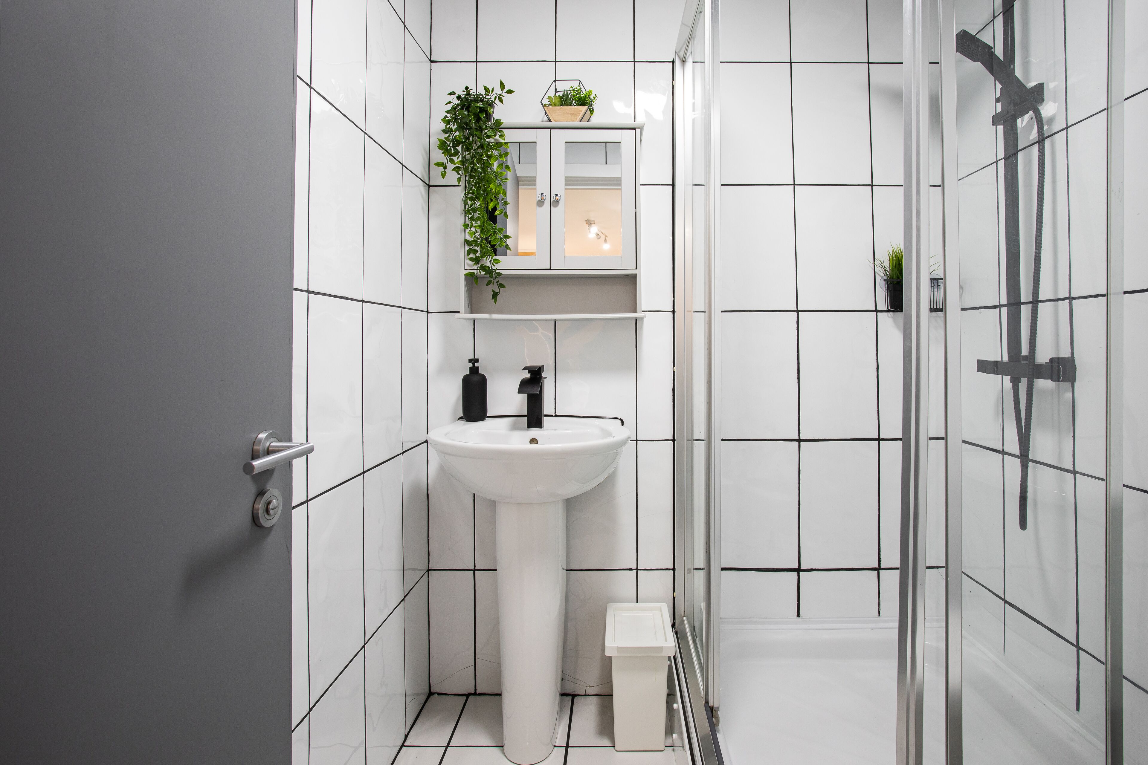 A modern bathroom with a white sink, a mirror, and a shower area.