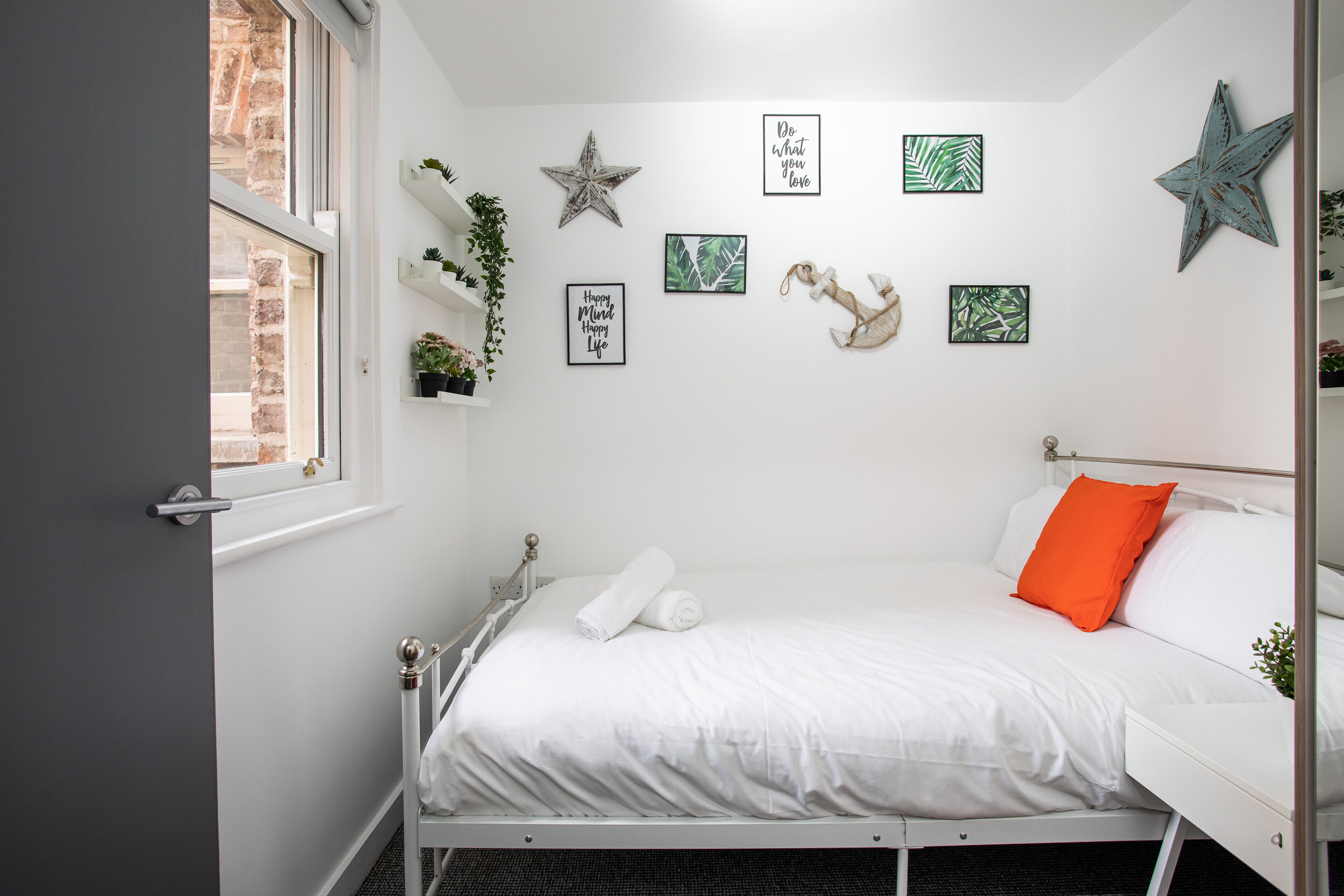 Un dormitorio ordenado con cama, ventana y adornos de pared, incluyendo estrellas y fotografías enmarcadas.