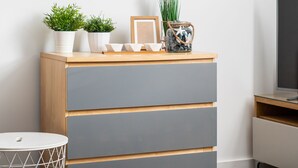 Une chambre moderne avec une commode en bois, des tiroirs gris et une petite table ronde. On peut voir des plantes en pot sur la commode et un tableau encadré au-dessus.