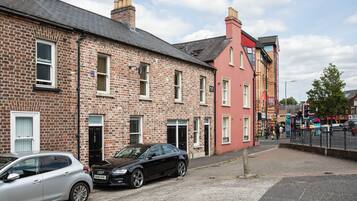 A street with brick houses, a black car parked on the side, and a pedestrian crossing.