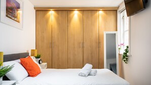 Une chambre d’hôtel avec un grand lit, une armoire en bois, une table de chevet avec une lampe et un téléviseur fixé au mur.