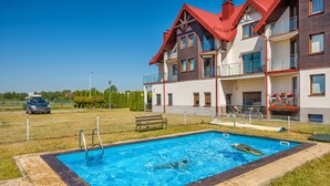 A residential building with a swimming pool, a fenced yard, and a parked car. - Apartamenty Sun & Snow Lisi Jar (Wladyslawowo)