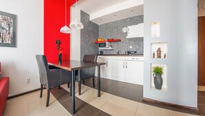 A modern kitchen with white cabinets, a red accent wall, and a dining area with a table and chairs. - Apartamenty Sun & Snow Lisi Jar (Wladyslawowo)