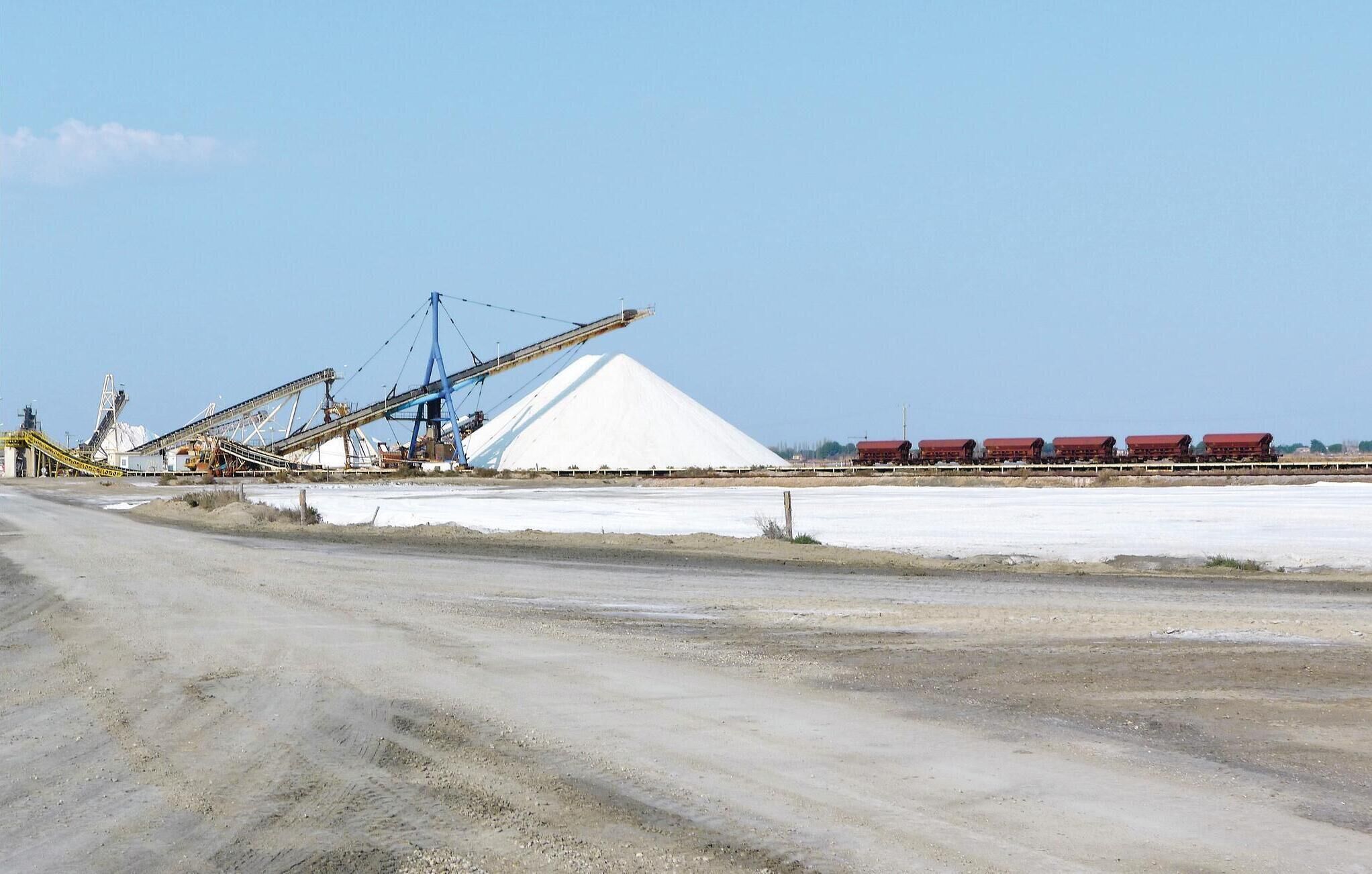 A large industrial facility with a conveyor belt system, a storage silo, and a train with red cargo cars.