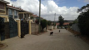 A residential street with houses, a paved road, and a clear sky. - Chester View Homestay - Hostel (Mlolongo)