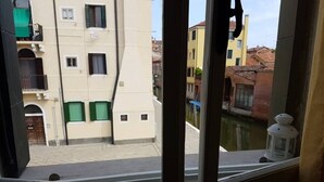 Blick aus einem Fenster auf eine Straße mit Gebäuden, einer Straßenlaterne und einem kleinen Gewässer.