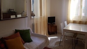 Ein Zimmer mit einem weißen Sofa, einem kleinen Holztisch, einem Fernseher und einem Spiegel an der Wand.