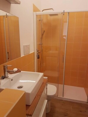 A bathroom with a white sink, a mirror, and a glass-enclosed shower area. - Grimaldi Apartments - Petit Maison (Venice)
