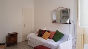 Ein Zimmer mit einem weißen Sofa, einem kleinen Holzschrank, einem Spiegel an der Wand und einer Pendelleuchte.