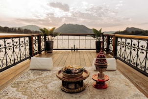 Un balcon offrant une vue sur la mer et les montagnes, agrémenté d’une table ornée d’un centre de table décoratif et de plantes en pot.