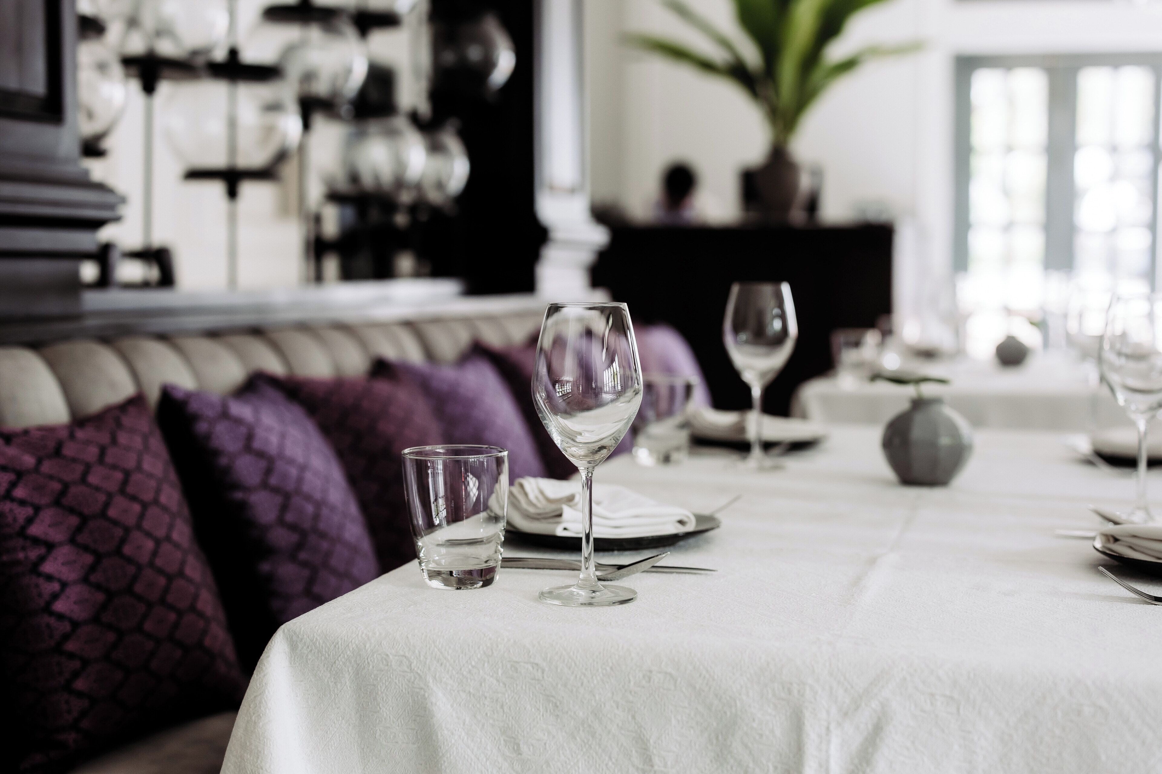 Una mesa de comedor cubierta con un mantel blanco, una copa de vino y un vaso de agua.