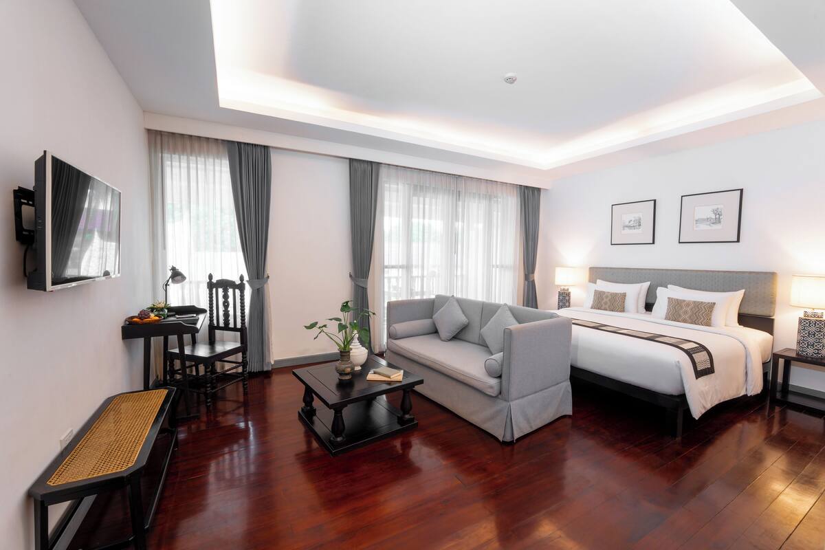 A modern hotel room with a bed, sofa, and a small dining area.
