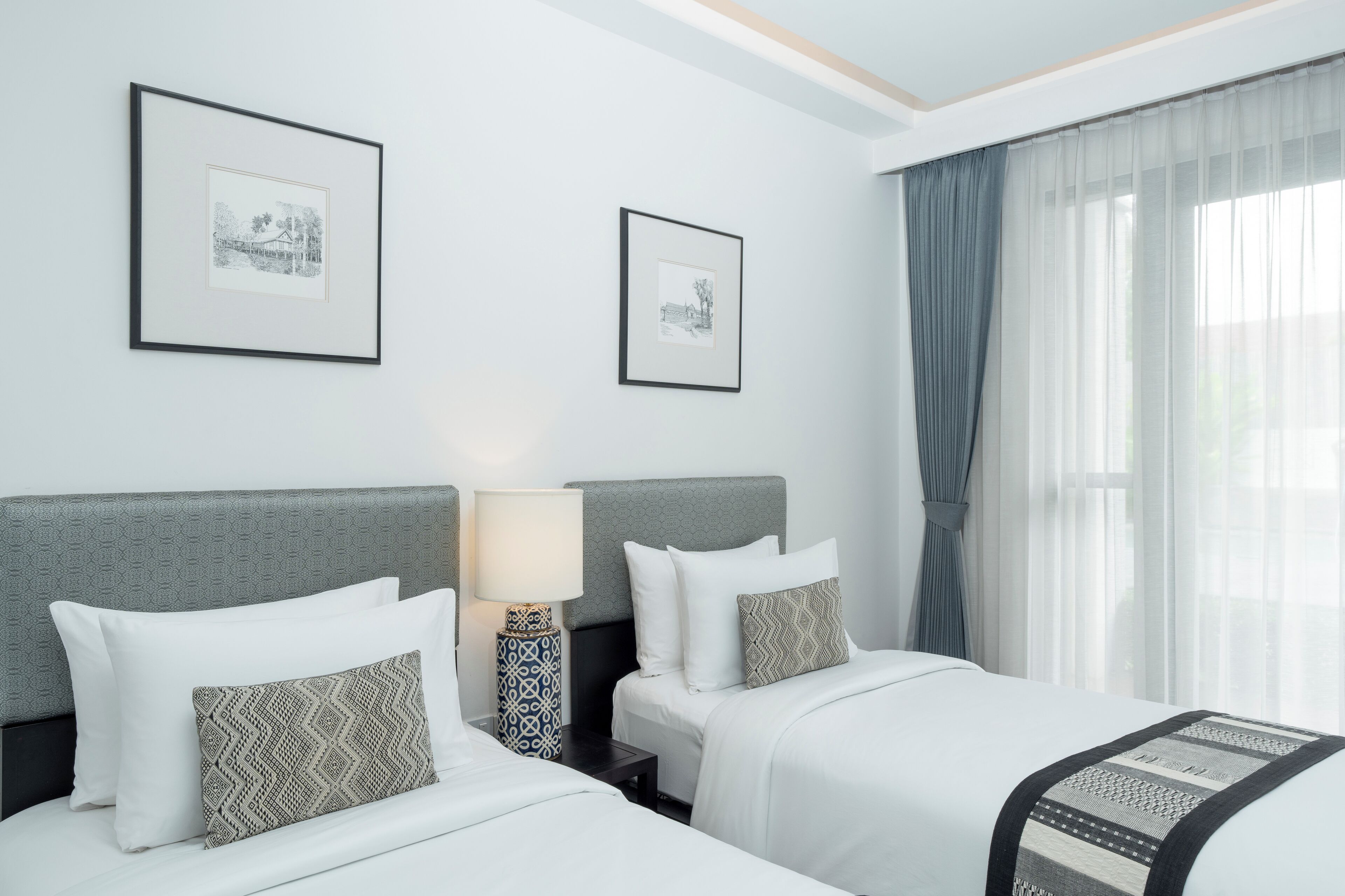 A hotel room with two beds, a nightstand with a lamp, and two framed pictures on the wall.