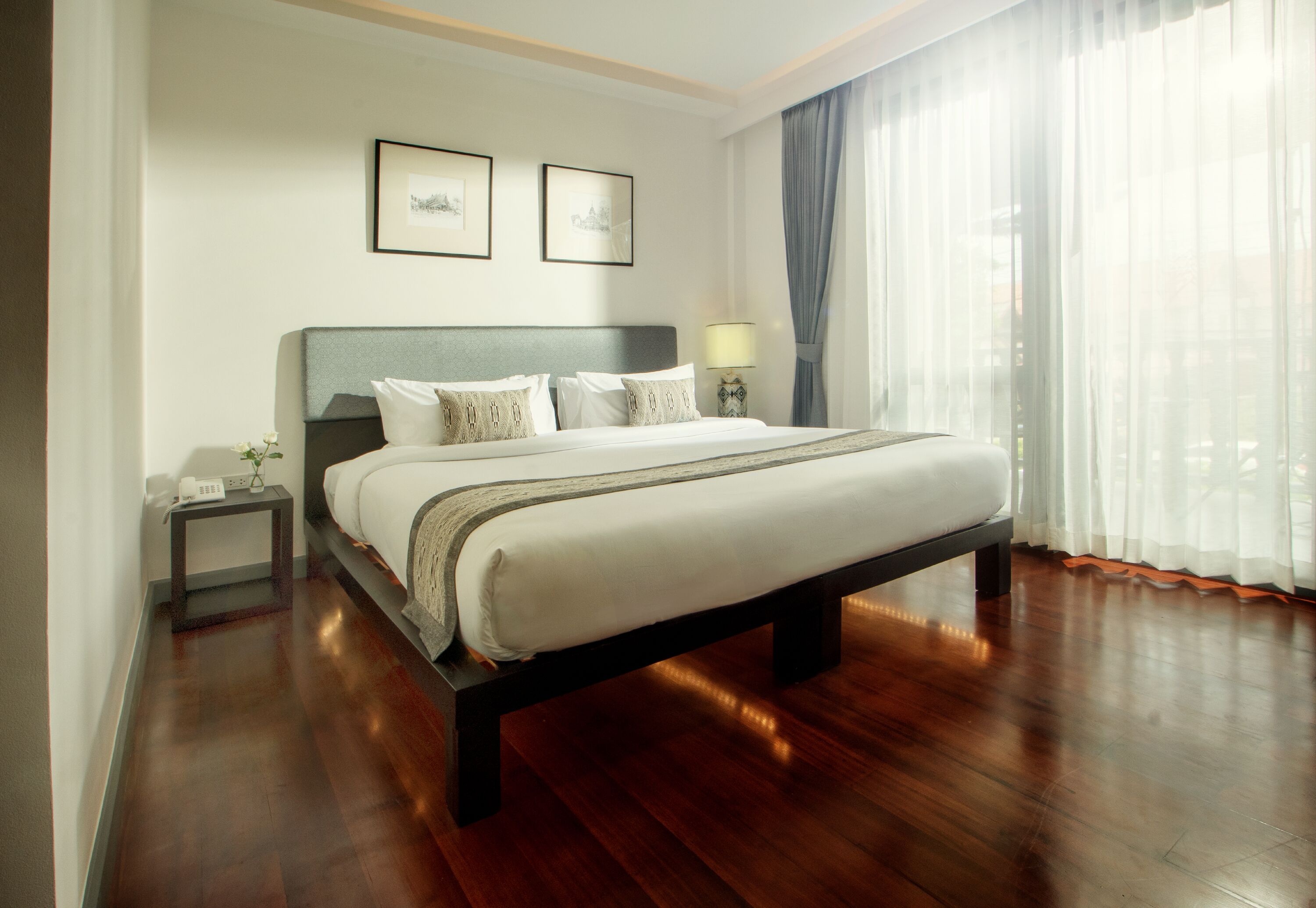 Un dormitorio ordenado con una cama grande, una mesita de noche con lámpara y dos cuadros en la pared.