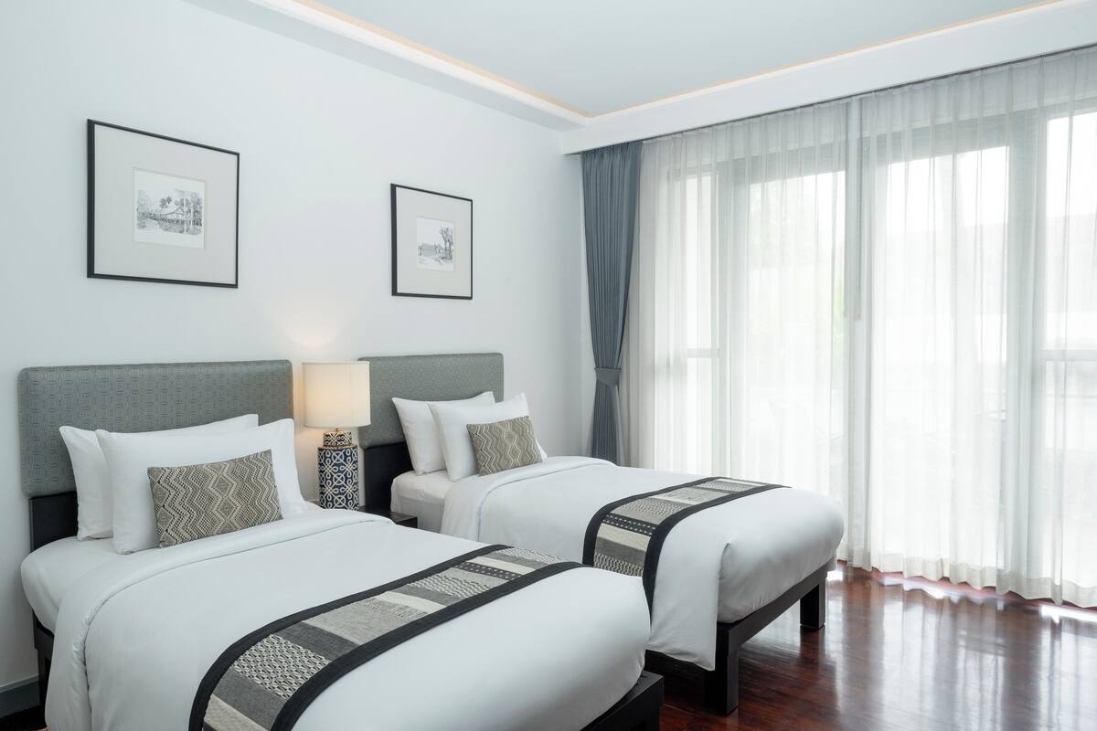 A hotel room with two beds, a nightstand, a lamp, and two framed pictures on the wall.