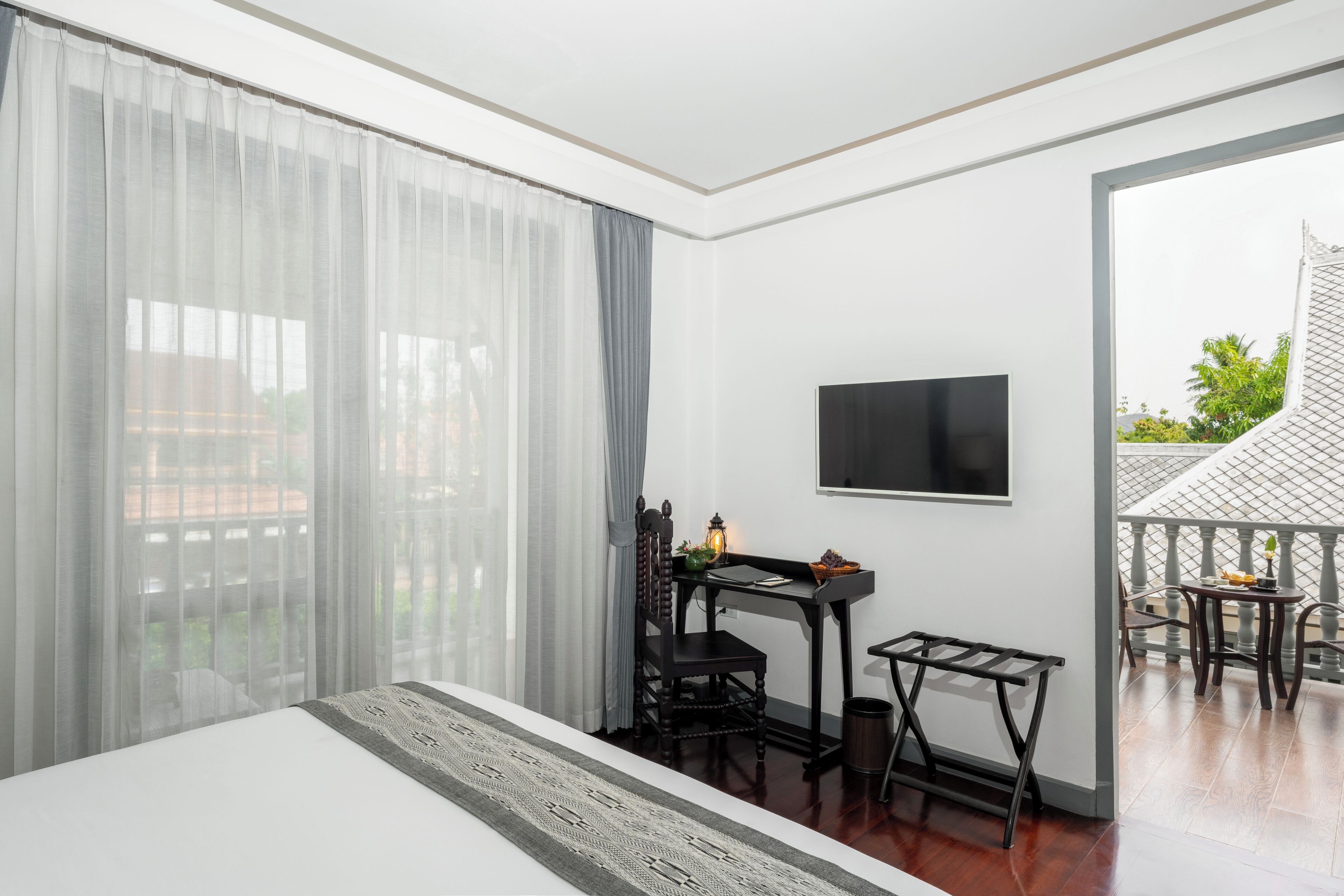 A modern hotel room with a large bed, a desk with a chair, a TV mounted on the wall, and a balcony with a view of the outside.
