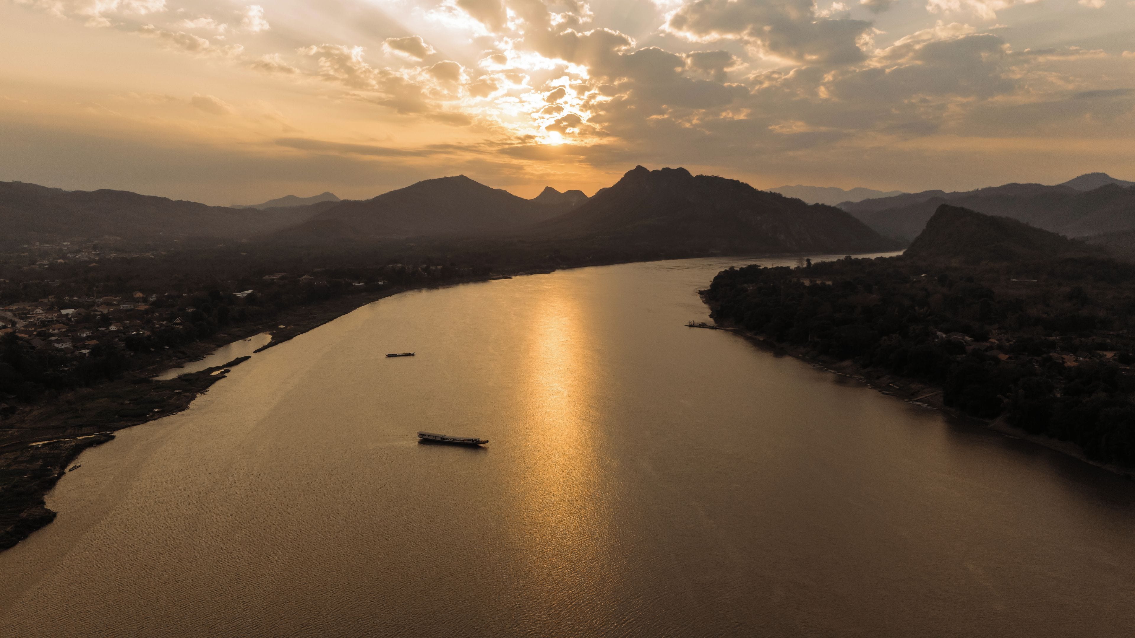 Um rio com barcos, cercado por montanhas e uma cidade.