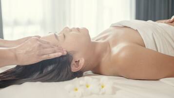 A person lying on a bed with white flowers, receiving a facial treatment.