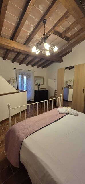 A bedroom with a bed, a wooden ceiling, a chandelier, a desk, and a mirror.