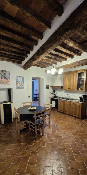A rustic kitchen with exposed wooden beams, a dining table with chairs, and a tiled floor.