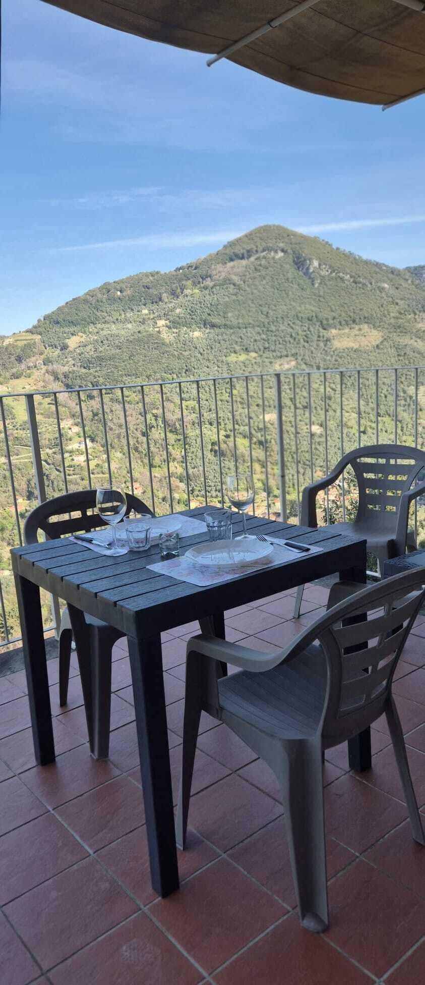 A terrace with a table and chairs, a view of a mountain, and a railing.