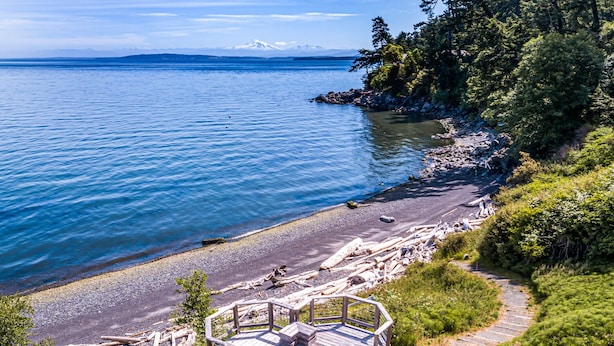 A wooden deck with a railing overlooking a rocky shoreline and a body of water. - Orcas Island, Mt. Baker Beach House, #289 (Eastsound)