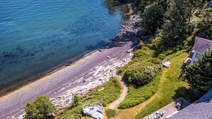 An aerial view of a coastal property with a beach, dense forest, and a clear view of the ocean. - Orcas Island, Mt. Baker Beach House, #289 (Eastsound)