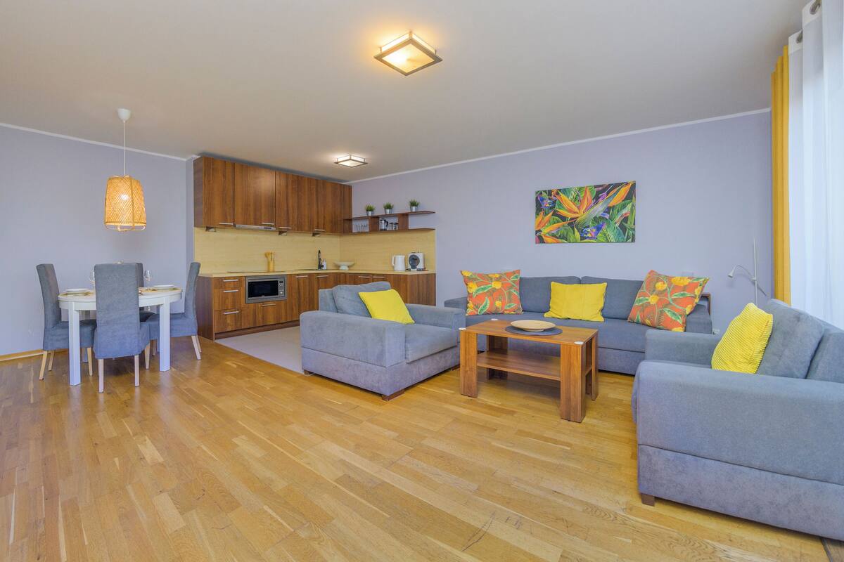 A modern living room with a grey sofa set, a wooden coffee table, and a dining area with a white table and grey chairs.