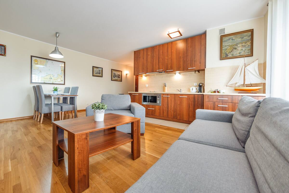 A modern living room with a sofa, a dining table, and a kitchen area with wooden cabinets and a stove.