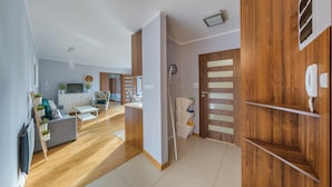 Una sala de estar moderna con un sofá, una mesa de centro y un televisor. Hay una puerta de madera con un teléfono y un interruptor de luz.
