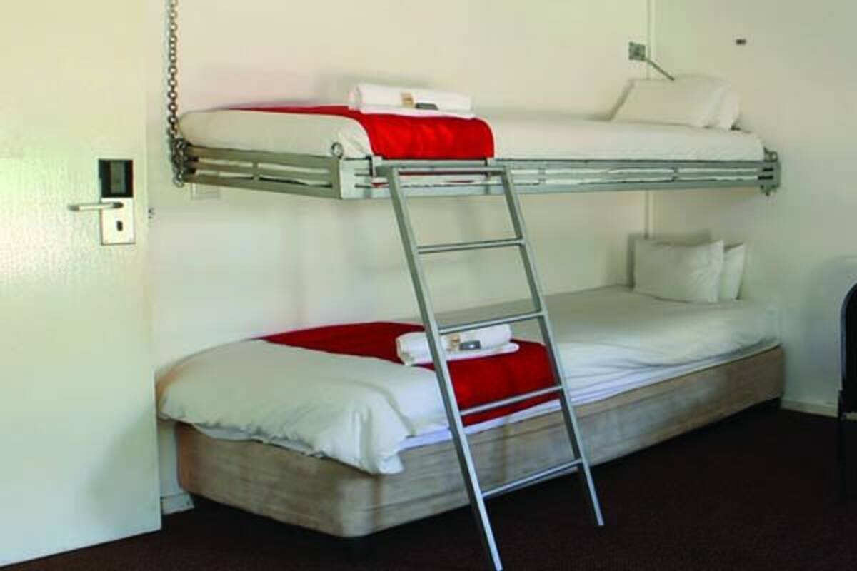 A room with bunk beds, a small table, a chair, and a shelf with a coffee machine.