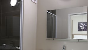 A bathroom with a glass shower enclosure, a sink with a mirror above it, and a trash can.
