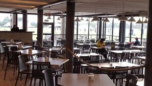 An indoor dining area with multiple tables and chairs, large windows, and a view of the outdoors.