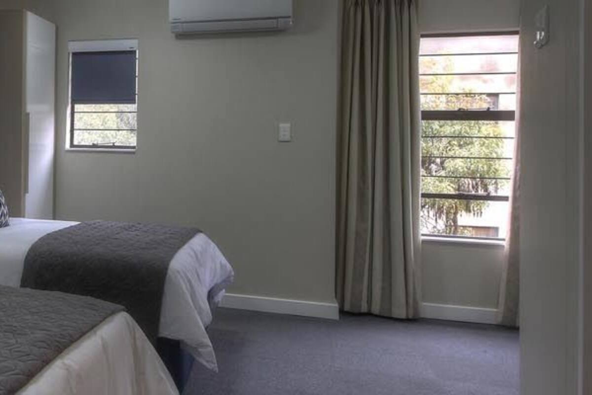 A hotel room with two beds, a window with curtains, and a door.
