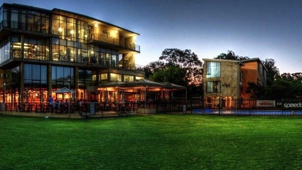 A modern building with multiple floors, large windows, and a well-maintained lawn in front.
