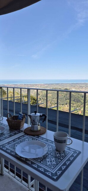 A balcony with a table set for two, overlooking a cityscape and the sea.