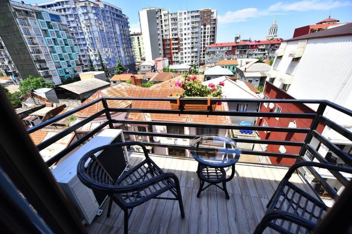 A balcony with a view of surrounding buildings, including a tall residential building and a smaller structure with a red roof.