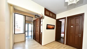 A hallway with wooden flooring, a large window, and a door with a sign. - Hotel Paliashvili (Batumi)