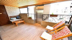 A balcony with a wooden floor, a bench, and two lounge chairs. - Hotel Paliashvili (Batumi)