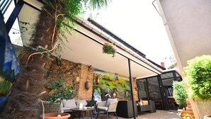 An outdoor patio with wicker furniture, a stone wall, and a mural. - Hotel Paliashvili (Batumi)