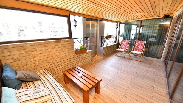 A balcony with a wooden floor, a sofa with striped cushions, a wooden table, and two chairs with red and white patterned cushions. - Hotel Paliashvili (Batumi)