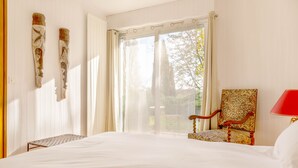 A hotel room with a large bed, a chair, a table, and a window with curtains. - La Maison de L'orbière (Forcé)
