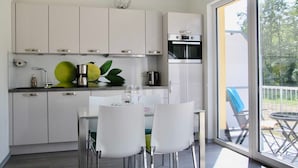 A modern kitchen with white cabinets, a dining table with chairs, and a view of the outdoors through large windows. - *öddeker, Lidia und Dieter GM 69137 - Holiday apartment in the coastal forest - Baltic Sea SNR: (Gelbensande)